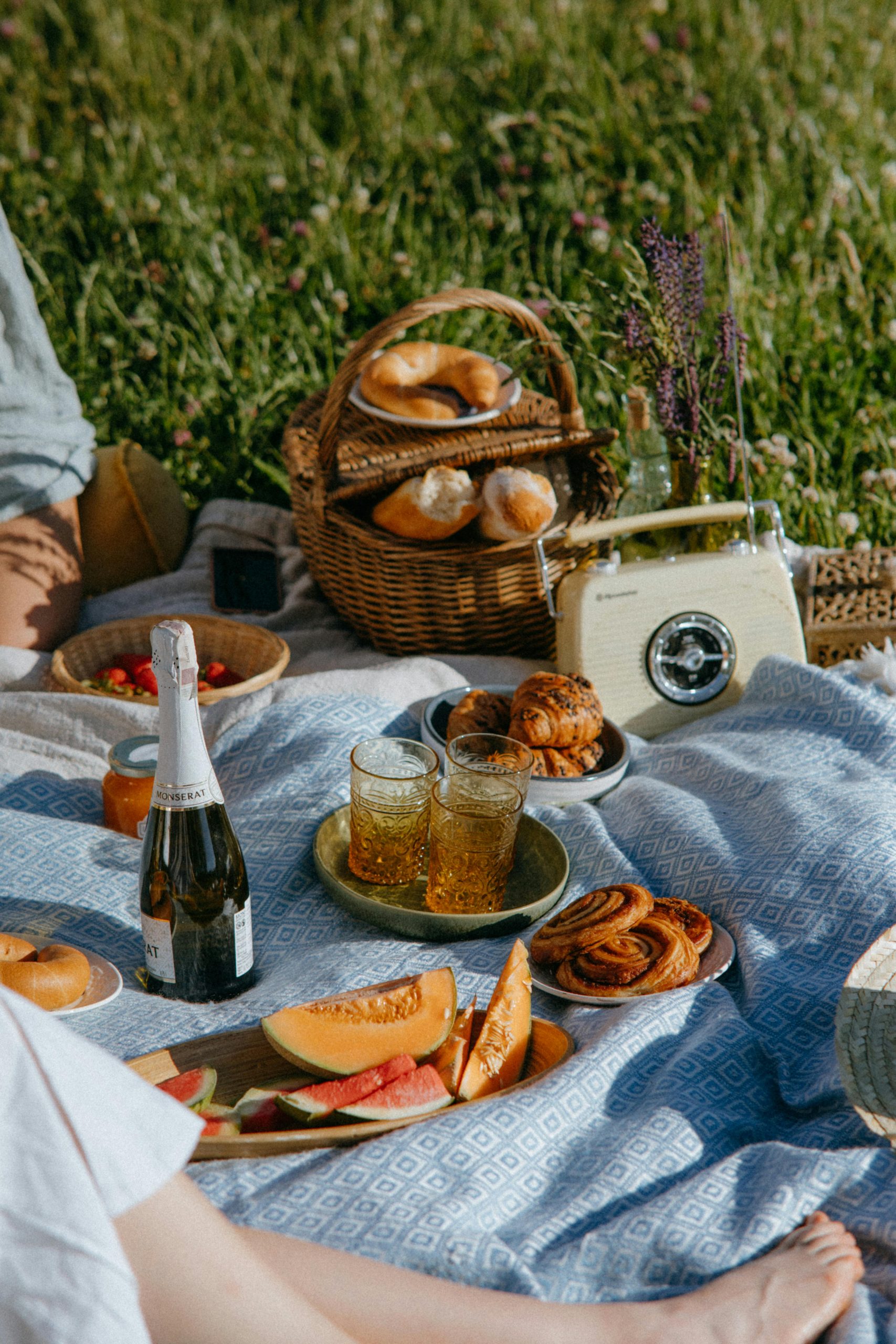 Enjoy a summer picnic with wine, fresh pastries, and fruit under the sun on a scenic field.